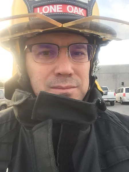 A firefighter wearing a hat and coat smiles at the camera.