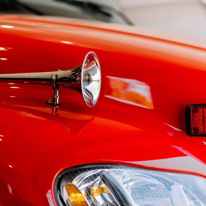 A horn is attached to the side of a red car.