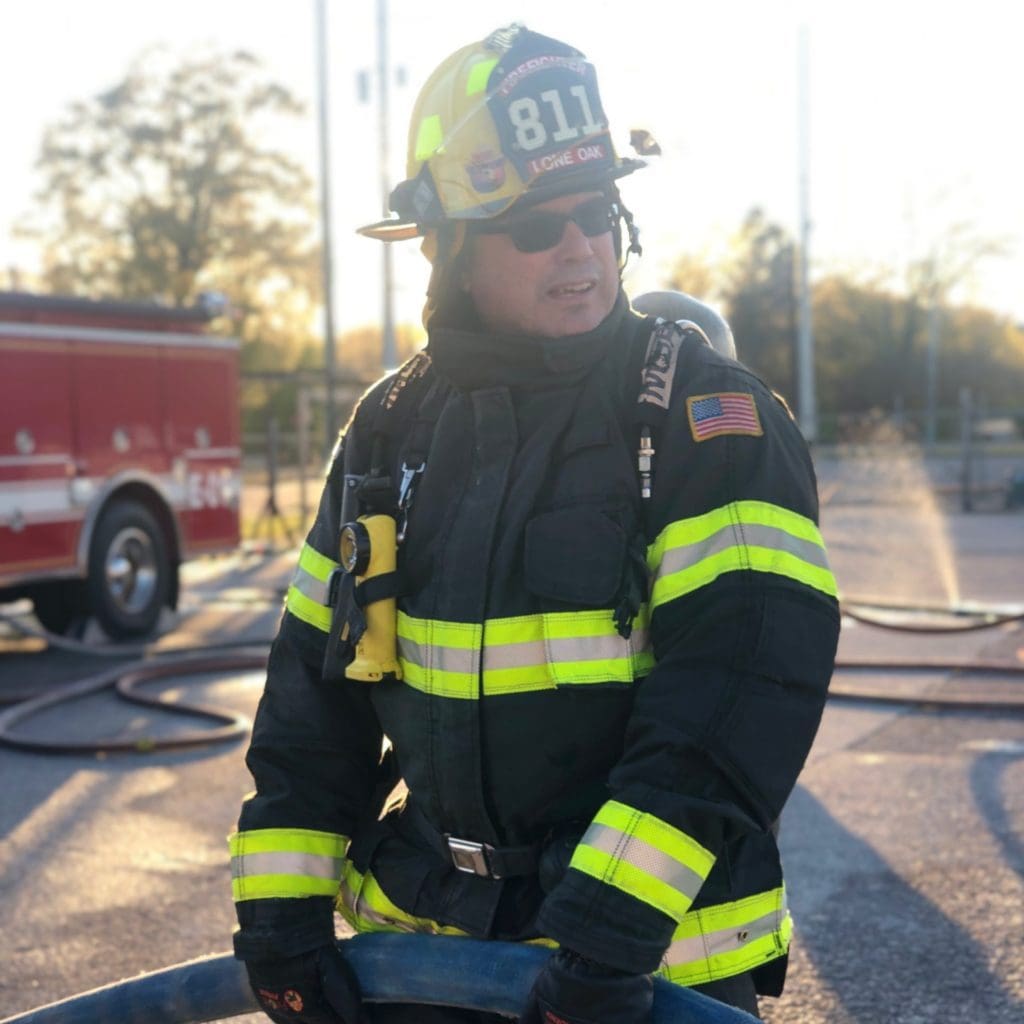 John R Kowalski is on site in full firefighter uniform holding a hose.