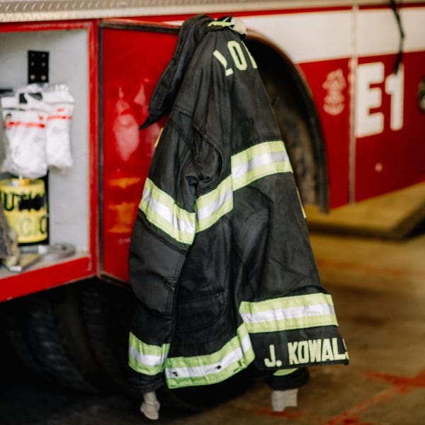 A firefighter's jacket hangs from a firetruck with the words "John R Kowalski" stitched on the bottom.